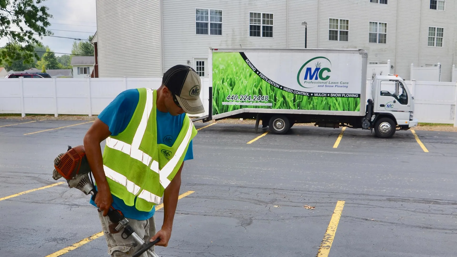 MC Professional Lawn Care and Snow Plowing expert is edging a lawn with a company truck parked behind him.